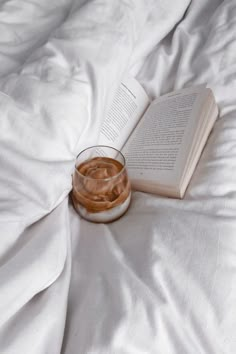 an open book sitting on top of a bed next to a glass filled with liquid