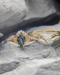 two gold rings with green and white stones on them sitting on top of some rocks