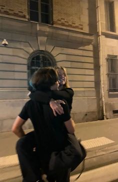 two people are hugging on the sidewalk in front of a building