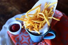 french fries on a plate with ketchup and mustard in a blue cup next to it