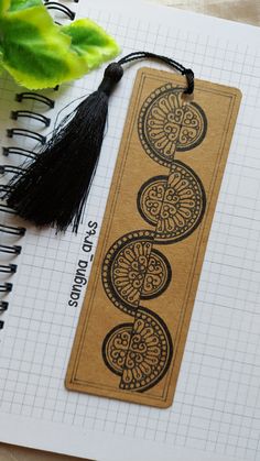 a bookmark with an intricate design on it next to a potted plant and notebook