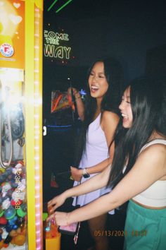 two young women are playing an arcade game at a carnival or party, and one is pointing her finger towards the machine