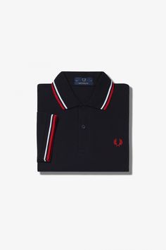 The original twin tipped Fred Perry Shirt. Made by expert hands in Leicester, England and adopting Fred's signature streamlined fit. A piece of British subcultural uniform for 60 years. Made in Leicester, England / Cotton piqué / Boxier fit than the M3600 with smart, flat hem / Twin tipped collar and cuffs / Two button placket COLOR: BLK/WHT/BT.RED Shirt Size S M L XL XXL Chest Size 35-37 38-40 41-43 44-46 47-49 Fred Perry Size 36 38 & 40 42 44 & 46 Classic Three-stripes Polo Shirt, Classic Three Stripes Polo Shirt, Classic Red Polo Shirt With Striped Collar, Classic Collared Tops With Contrast Stripes, Classic Tops With Contrast Stripes And Collar, Classic Navy Polo Shirt With Contrast Collar, Classic Navy Polo Shirt With Contrast Trim, Classic Navy Tops With Contrast Trim, Navy Classic Tops With Contrast Trim