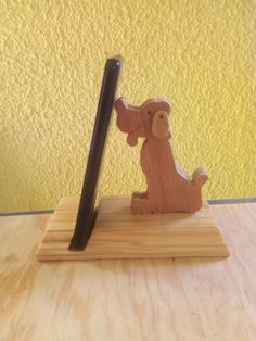 a wooden toy dog holding a stick on top of a wood stand with a yellow wall in the background