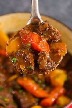 a spoon full of beef stew with carrots and potatoes on it, in a red pot