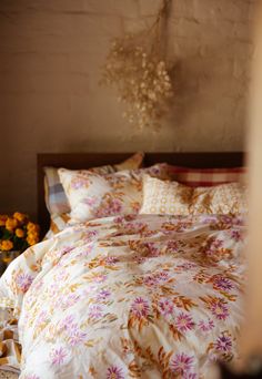 a bed with white and pink flowers on it next to a vase filled with yellow flowers