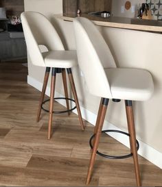 three white bar stools sitting in front of a counter top with a wooden base