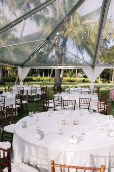 tables and chairs are set up under a tent for an outdoor wedding reception with palm trees in the background