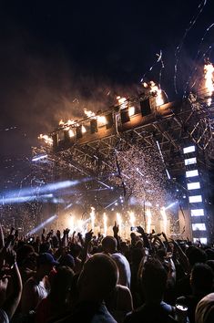 a large group of people at a concert with their hands in the air and lights on