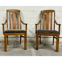 two wooden chairs side by side against a white brick wall with black and green cushions