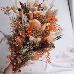 a person holding a bouquet of flowers in their hand on top of a white sheet