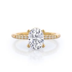 a yellow gold engagement ring with an oval cut diamond in the center and pave set shoulders