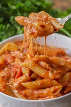 a spoon full of pasta with sauce and parsley in the background, on top of a white bowl