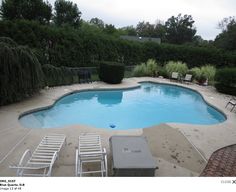 an empty swimming pool with lawn chairs around it and trees in the backround