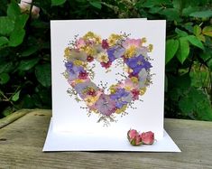 a card with flowers in the shape of a heart on top of a wooden table