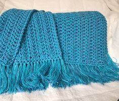 a blue knitted blanket laying on top of a bed