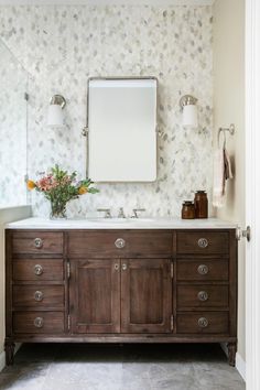 a bathroom vanity with two sinks and a large mirror above it, in front of a floral wallpapered wall