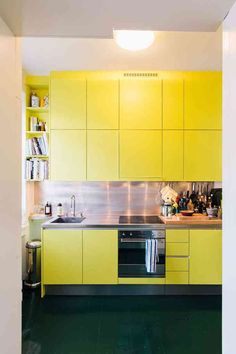 a kitchen with yellow cabinets and green flooring in the center is an open door leading to another room