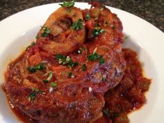 a white plate topped with meat covered in sauce and garnished with parsley