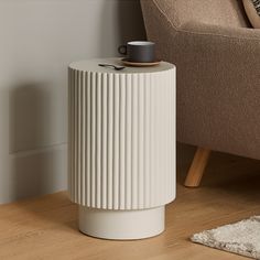 a white table with a cup on it next to a brown chair and rugs