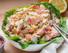 a white bowl filled with chicken salad next to some dipping sauce and lemon wedges