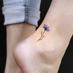 a small blue flower tattoo on the left side of the foot is shown in front of a woman's right leg