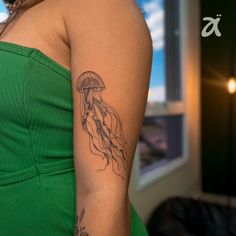 a woman wearing a green dress with a tattoo on her arm that has a jellyfish in it