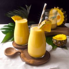 two glasses filled with yellow liquid next to pineapples