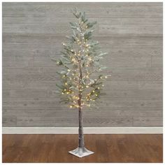 a small white christmas tree with lights on it's branches in front of a wooden wall