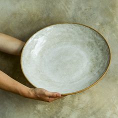 a person holding a white plate on top of a cement floor next to a wall