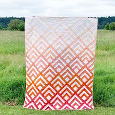 an orange and white quilt sitting on top of a lush green field next to tall grass