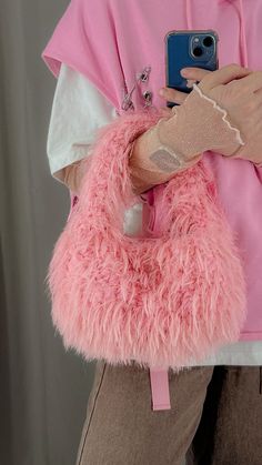 a woman in pink is holding a cell phone and wearing a fuzzy pink bag with her hand on the shoulder