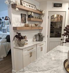 a white kitchen with marble counter tops and shelves on the wall above it is an open door leading to a bedroom