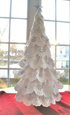 a white christmas tree sitting on top of a red table cloth next to a window