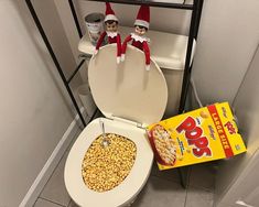 two elfs sitting on top of a toilet with cereal in front of it and a box of pop