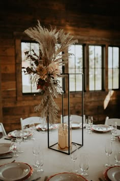 a table set with plates, silverware and tall centerpieces in front of windows