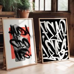 two framed art pieces with graffiti on them in front of a potted plant and window