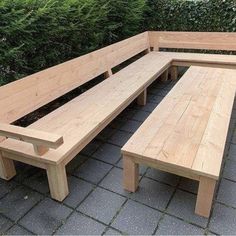 a wooden bench sitting on top of a sidewalk next to green bushes and shrubbery