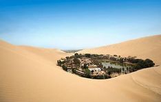 an aerial view of a desert resort surrounded by sand dunes and green trees in the distance