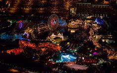 an aerial view of a city at night with ferris wheel in the foreground and lights all around