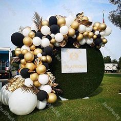 an arch made out of balloons and palm leaves on the grass with a sign in the background