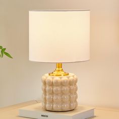 a white lamp sitting on top of a table next to a book and potted plant