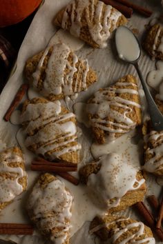 cinnamon rolls with icing and cinnamon sticks are on a tray next to an orange pumpkin