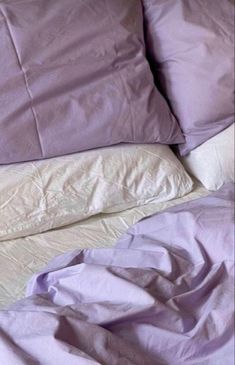 an unmade bed with purple sheets and pillows