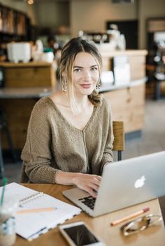 a woman sitting at a table with a laptop computer in front of her, smiling