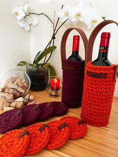 three wine bottles in knitted bags on a table with candles and flowers behind them