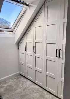 an attic bedroom with white closets and skylight in the ceiling, along with carpeted flooring