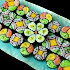 there are many colorful sushi rolls on the blue platter with yellow and green toppings