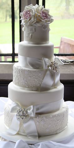 a three tiered wedding cake with white ribbons and bows on it's side