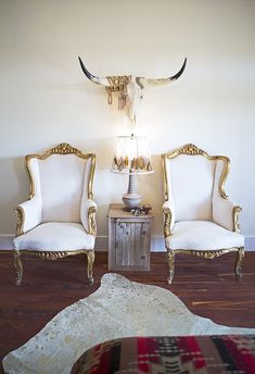 two white chairs sitting next to each other on top of a hard wood floor in front of a cow skull